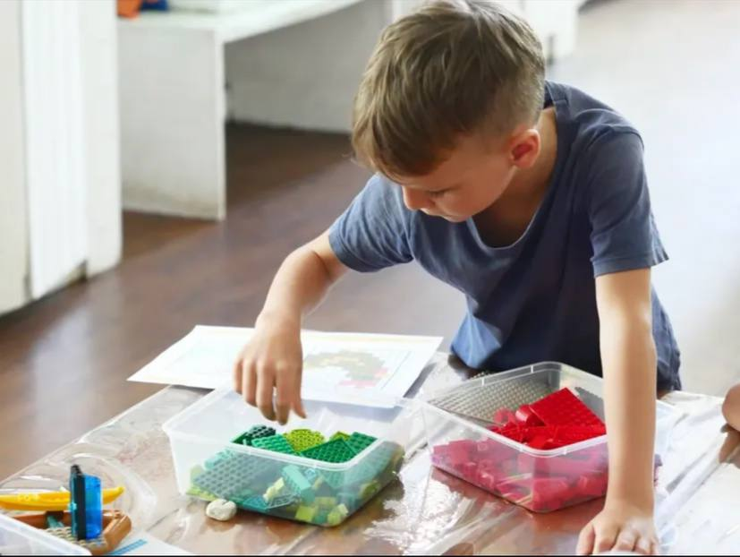 Ребенок сидит за столом и собирает конструктор Lego из прозрачных контейнеров